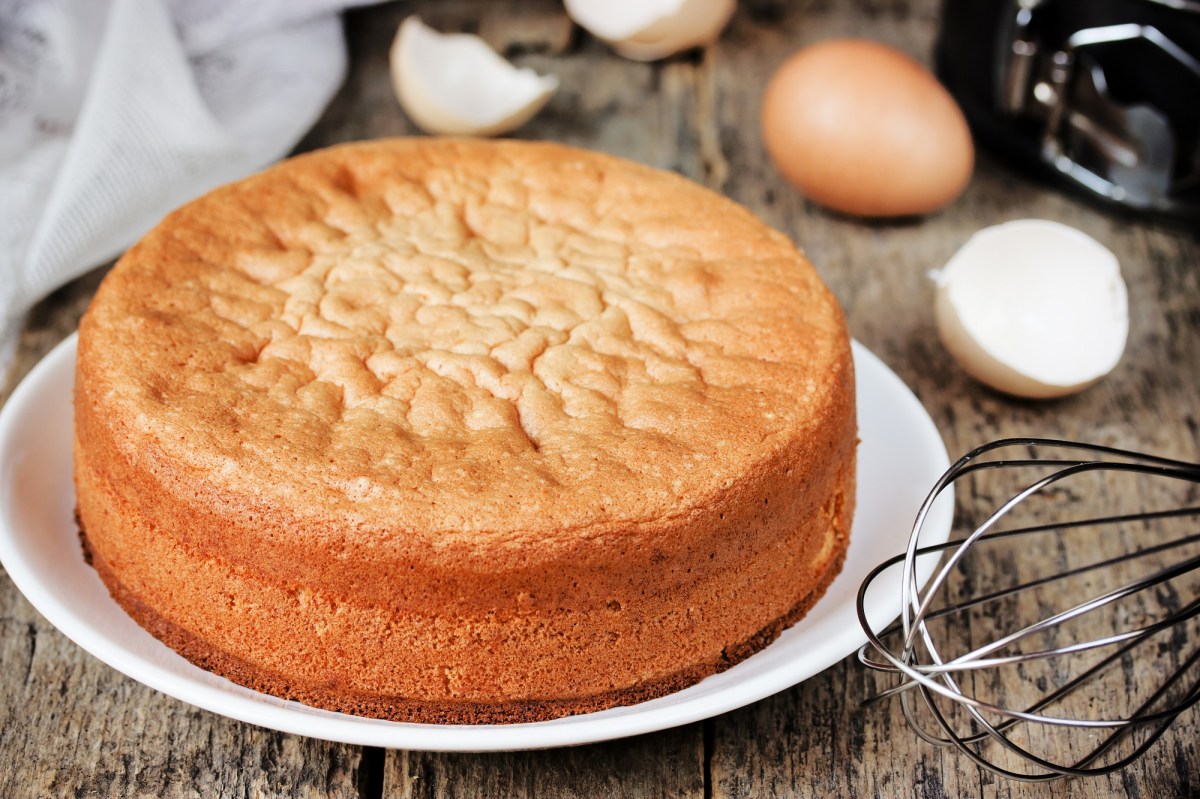Pastel de mazapán de dos ingredientes en un plato blanco. Detrás hay cáscaras de huevo y un batidor.
