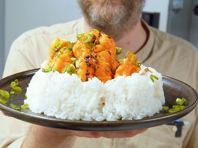 Un plato con una porción grande de arroz, sobre el cual se distribuyen los camarones Bang Bang. El chef Oli sostiene el plato hacia la cámara.