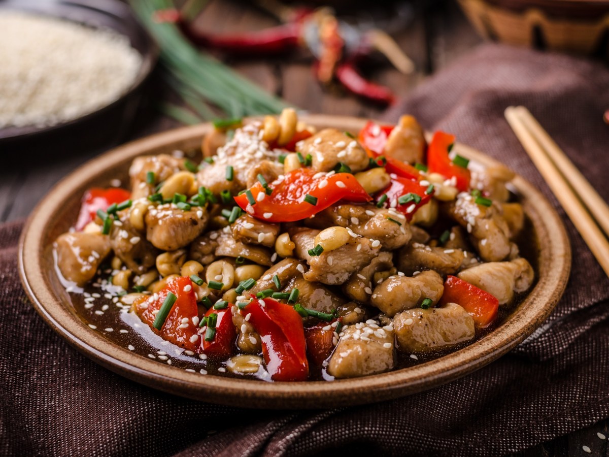 Pollo Kung Pao en un plato marrón claro. Junto a él hay palillos