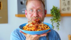 El cocinero Oli sostiene un plato de Bucatini all'Amatriciana hacia la cámara.